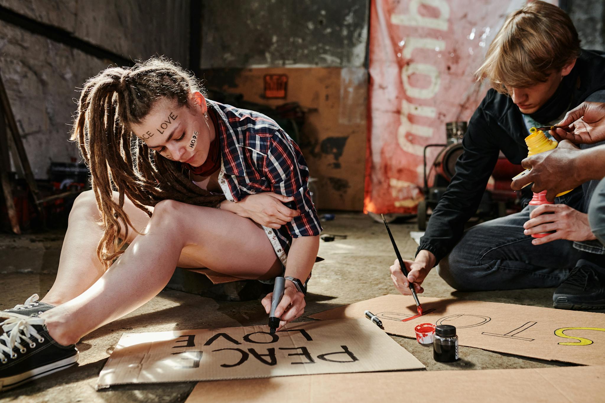 Group of activists creating protest signs with paint on cardboard indoors, expressing peaceful messages.